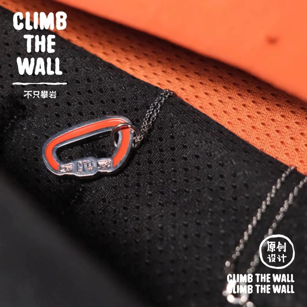 Close-up of a black and orange climbing harness with a carabiner, featuring 'Climb the Wall' branding.