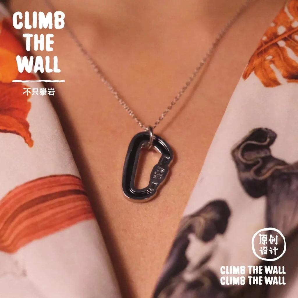 Black carabiner pendant necklace on a person wearing a patterned shirt with 'CLIMB THE WALL' branding.