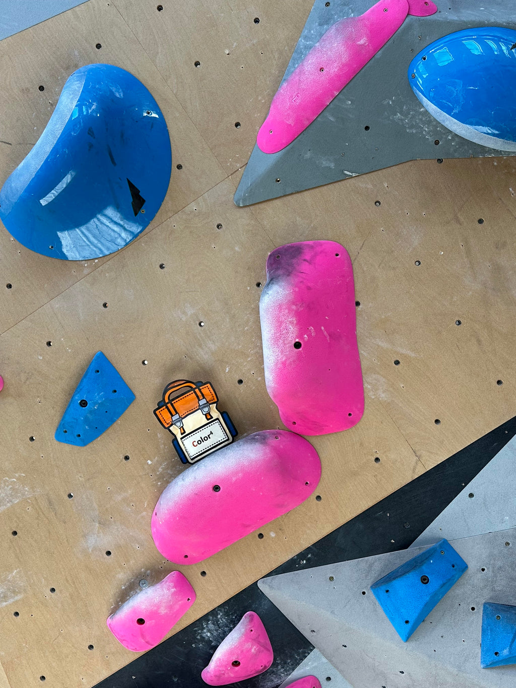 Colorful climbing holds on a wooden climbing wall with a small backpack pin.
